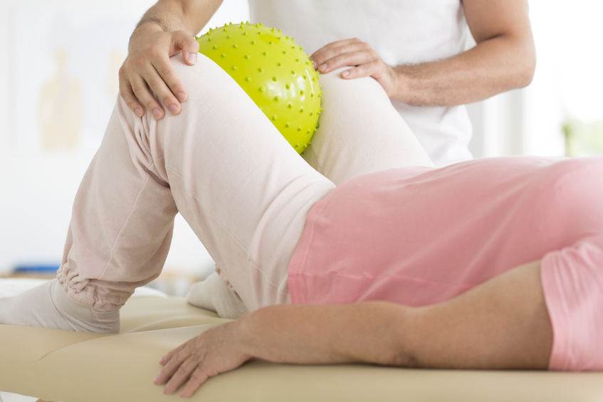 Hip Adductor Exercise With A Ball | Dr Ken Nakamura Best Toronto Chiropractor close-up of patient holding yellow ball between her knees during rehabilitation